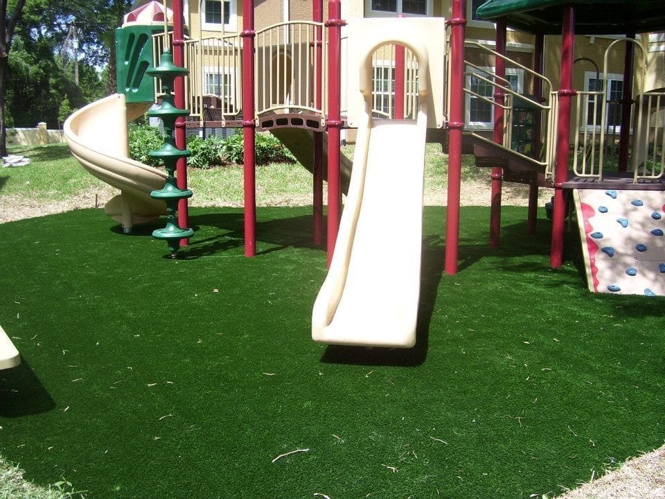 Empty playground slide on green artificial grass under sunlight.
