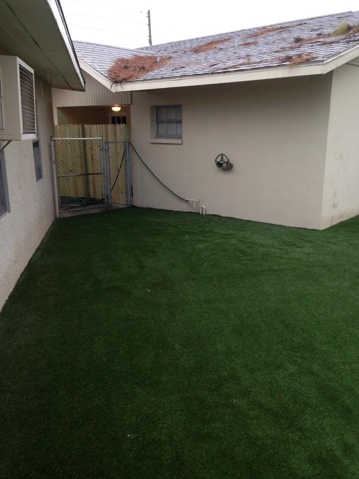 A small backyard with artificial green grass between two buildings.