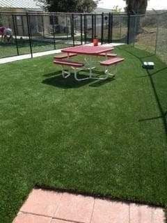 Picnic table on well-maintained artificial grass in fenced area.