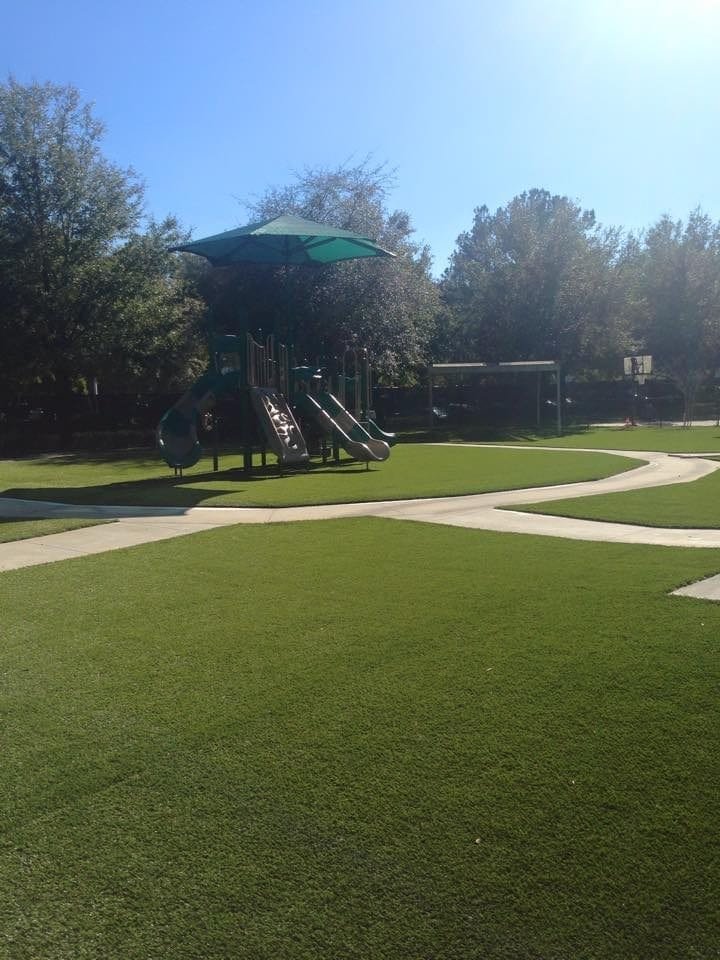 Playground with green turf and a play structure under a clear sky.