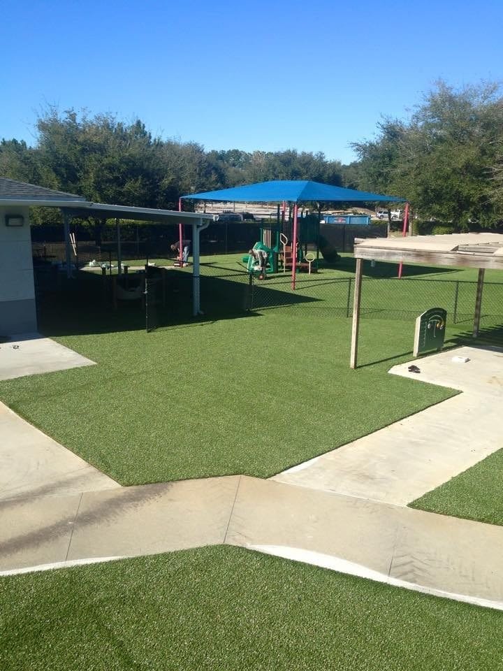 A clean outdoor playground with artificial turf and shade structures.