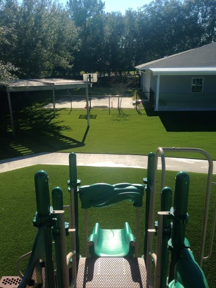 A playground slide with a green lawn and residential houses in the background.