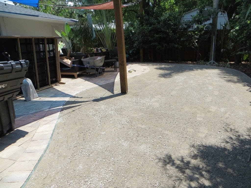 A sunny backyard with gravel ground and some shadows from trees.
