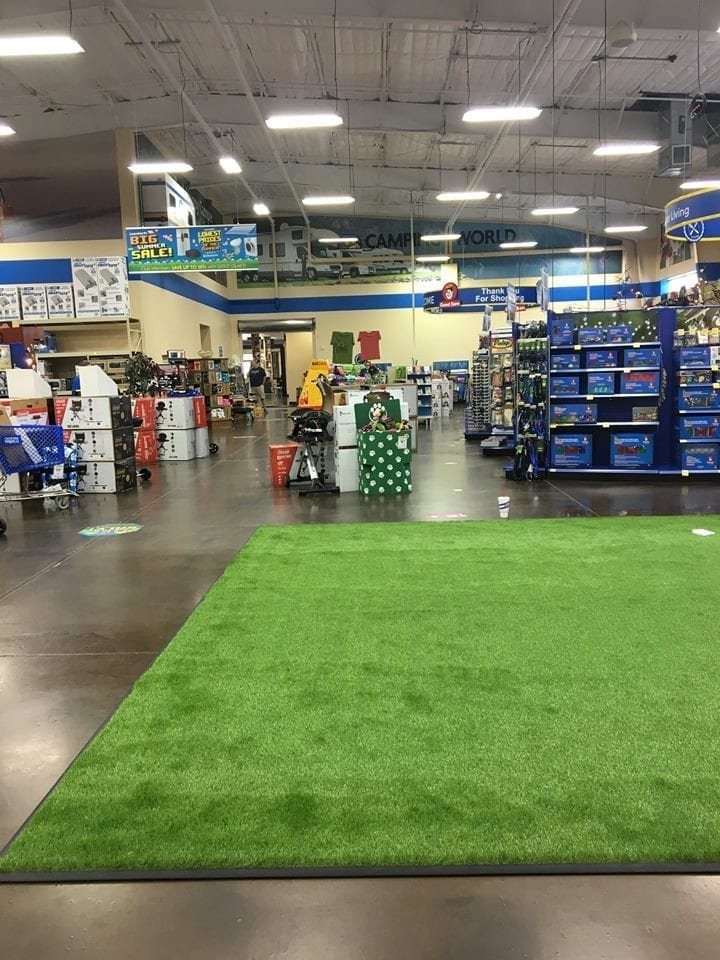 Indoor store aisle with artificial grass and shelves of products.