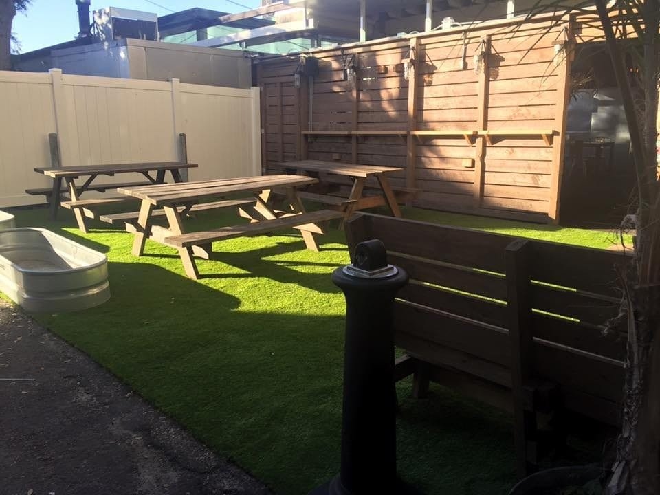 Sunlit backyard with picnic tables and artificial grass under clear sky.