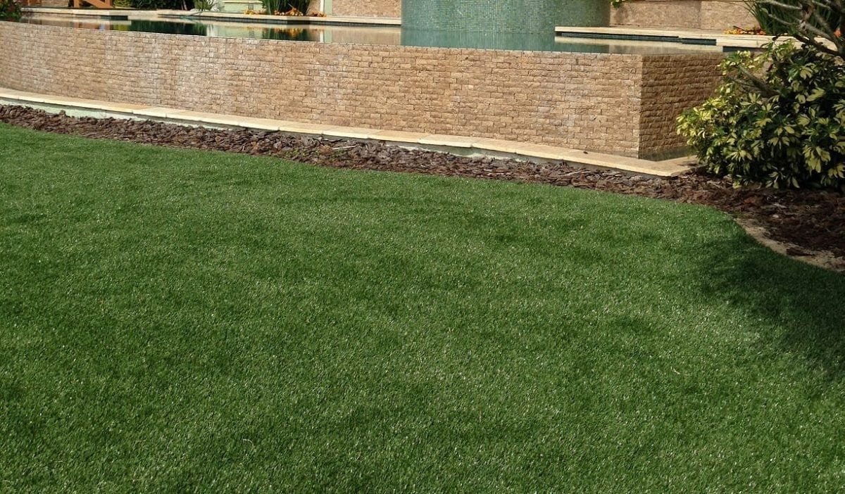 A well-maintained green lawn bordered by a stone wall and a brick structure.