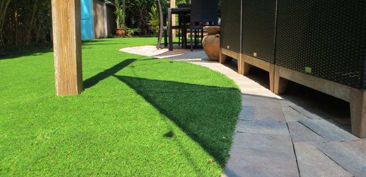 Curved artificial grass lawn with shadow and patio furniture.
