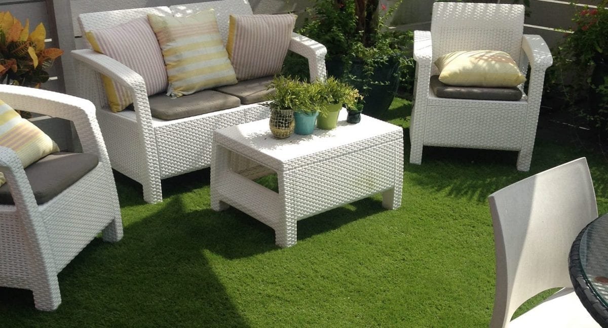 White wicker outdoor furniture set on green grass with potted plants.