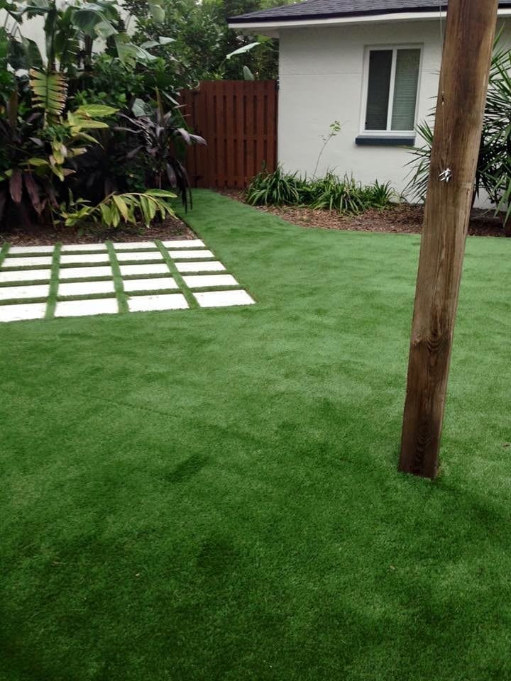 A green lawn with stepping stones and a tree trunk near a wall.