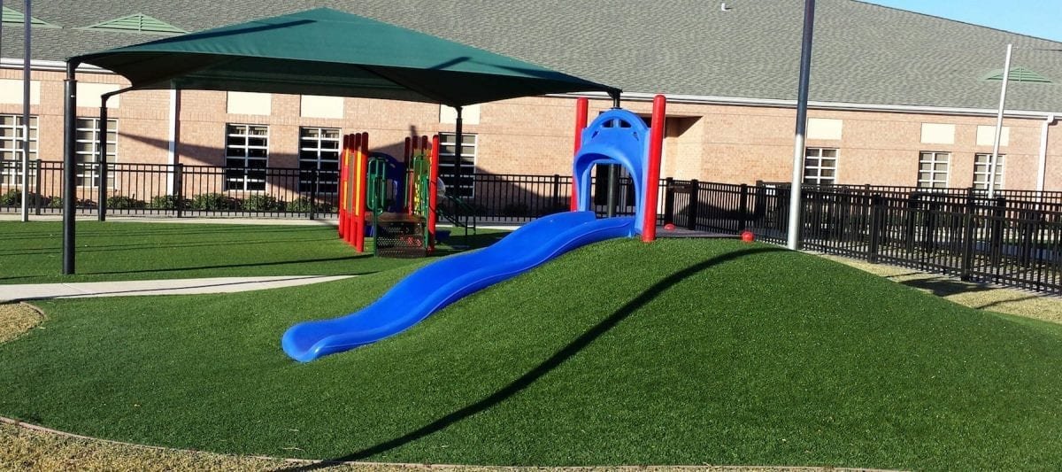 Blue slide on artificial grass in a sunny playground.