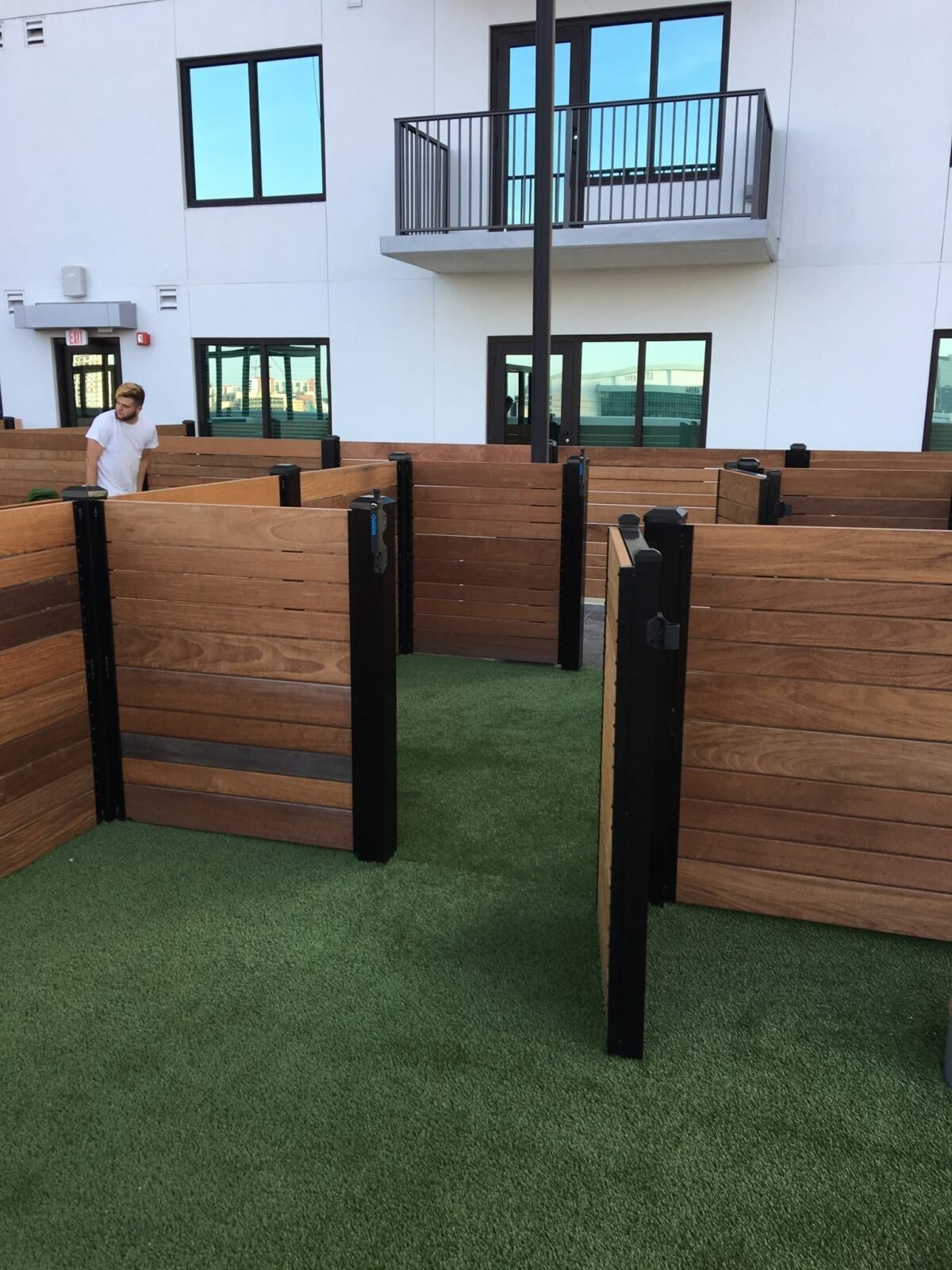 Outdoor wooden partitions with black frames on artificial grass in front of a building.