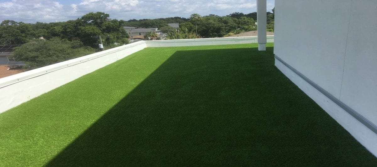 A sunlit patio with artificial grass and a scenic view.