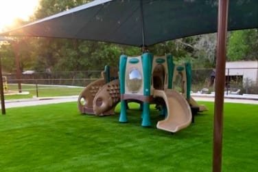 A small playground with a slide and climbing features on artificial grass.