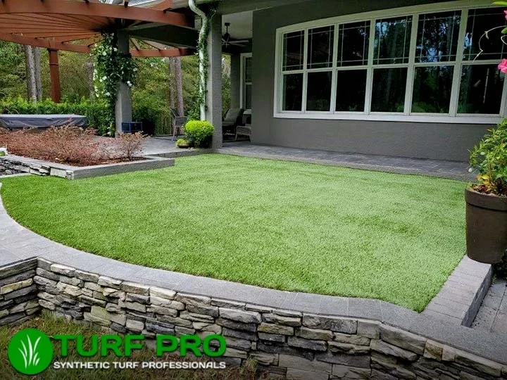 A neatly manicured artificial turf lawn bordered by stone and flower beds.