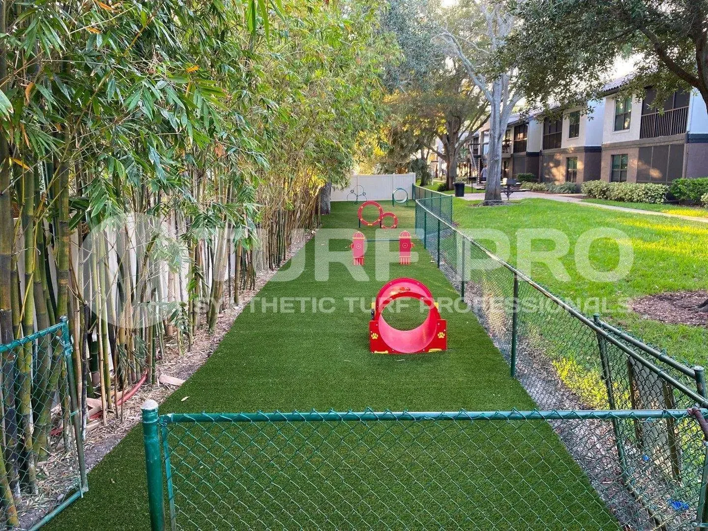 A fenced outdoor area with artificial grass and a red tunnel toy for pets.