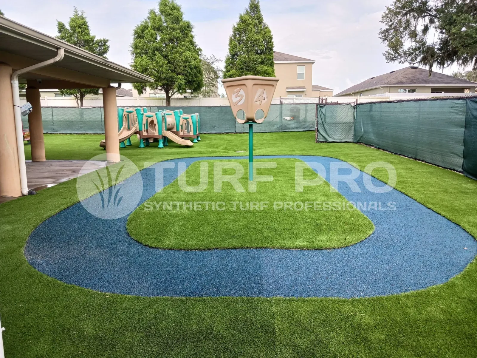 A synthetic turf basketball court with a modern hoop setup and surrounding residential buildings.