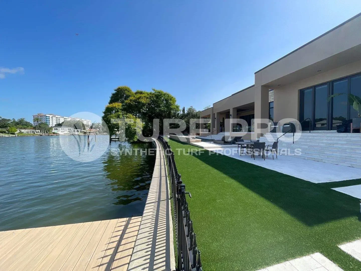 Modern house with a waterfront view and manicured lawn under a clear blue sky.