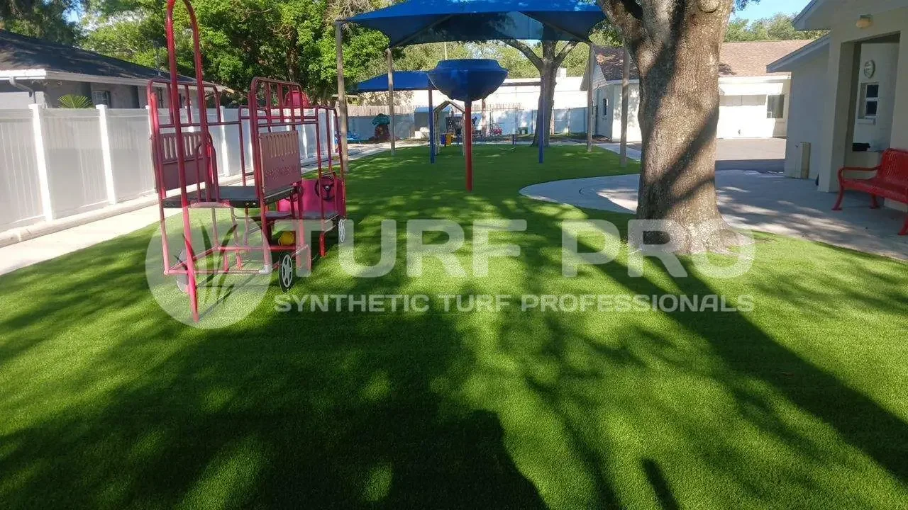 Artificial turf installed around a playground area with trees and shadows.