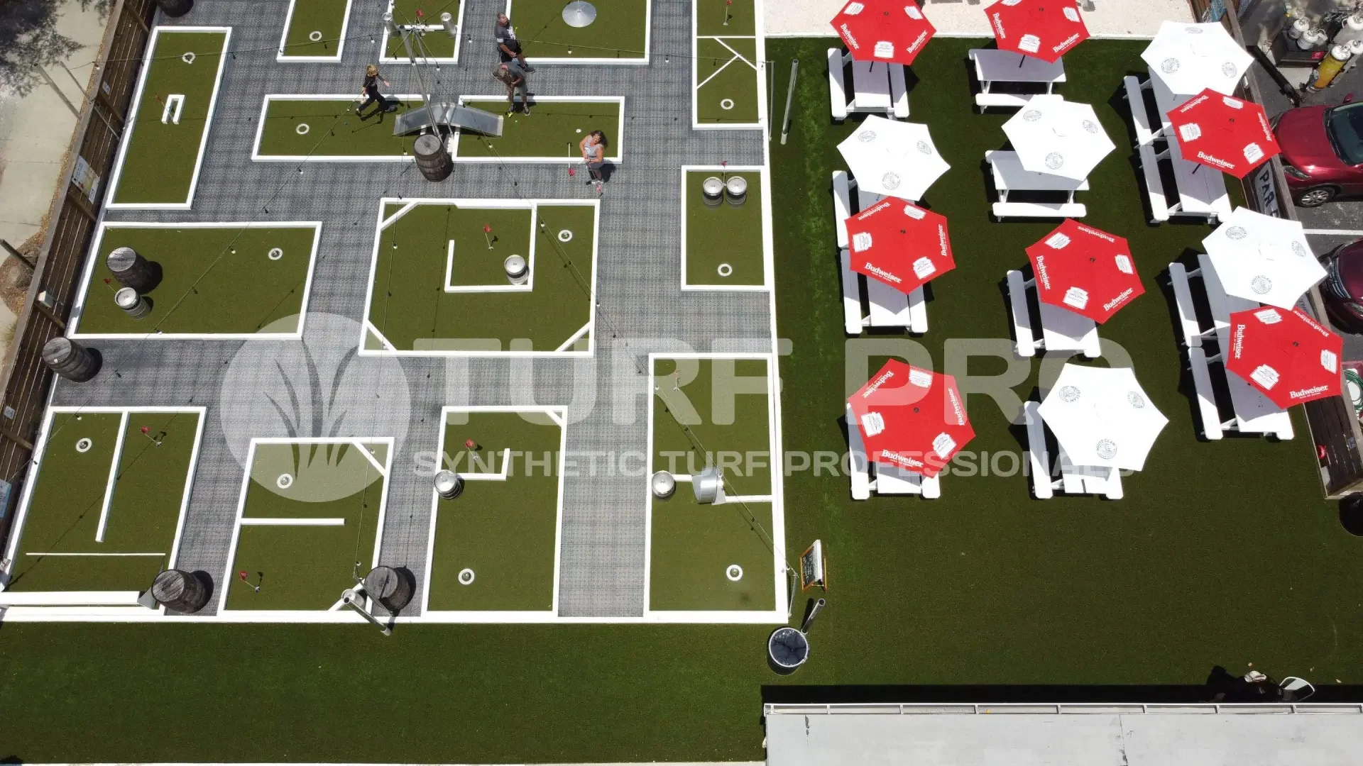 Outdoor miniature golf course with red and white umbrella-covered tables.