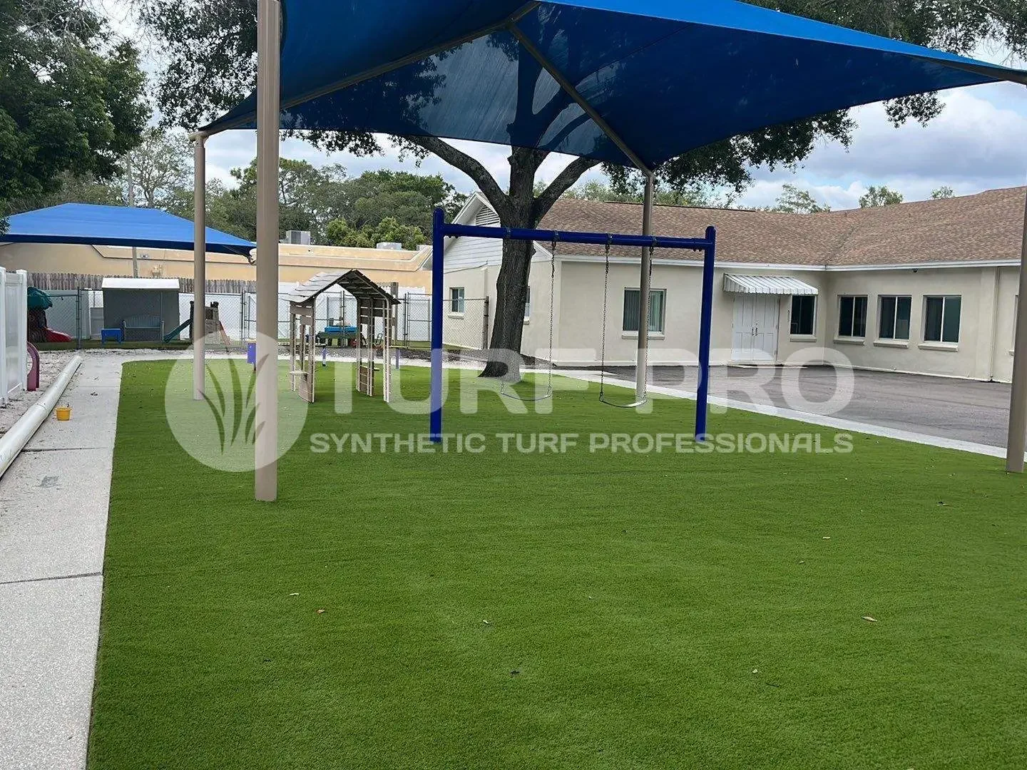 Playground swing set on synthetic turf under shade sails.