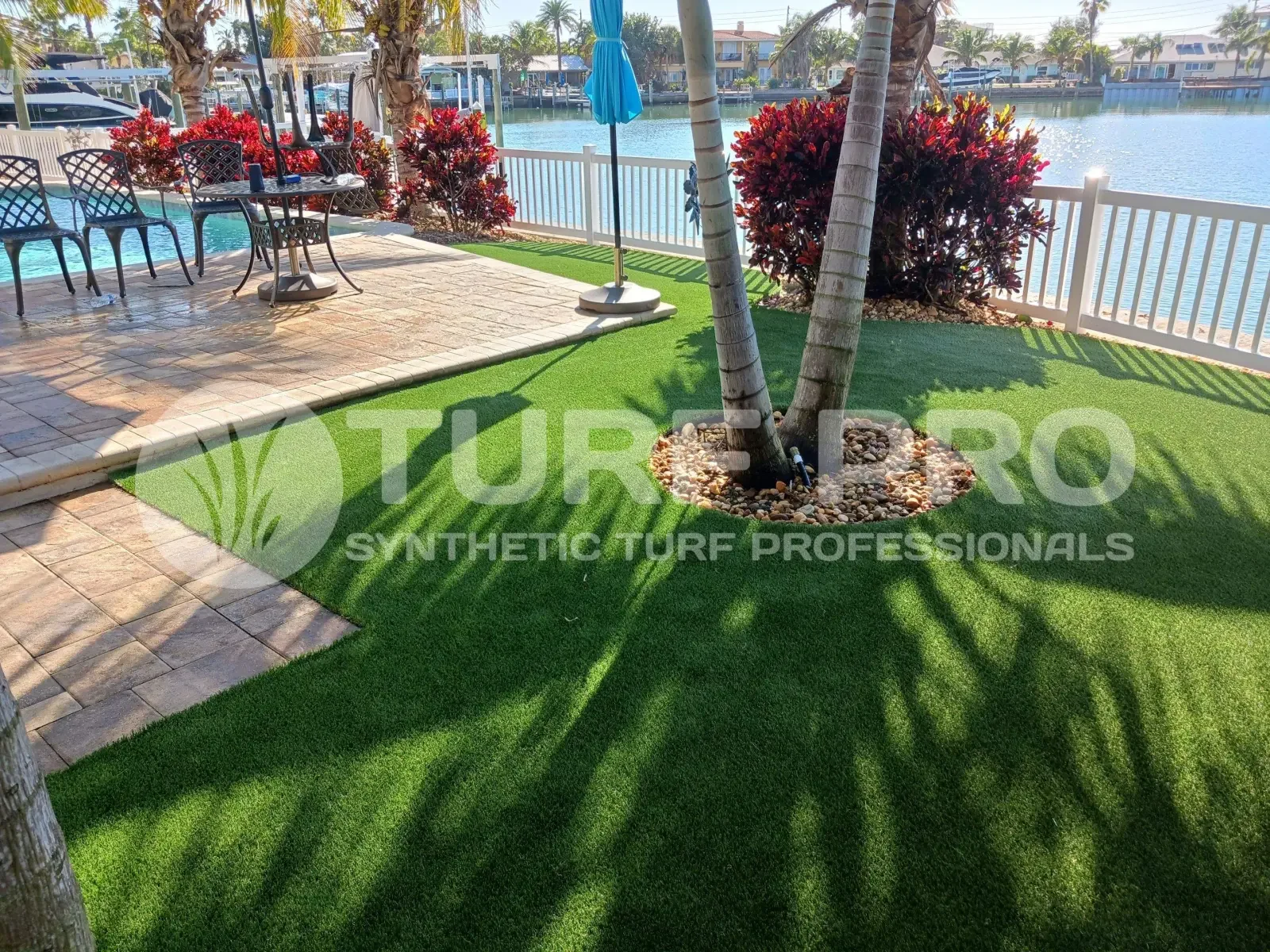 Well-maintained backyard with green grass, palm tree, and outdoor seating by the water.