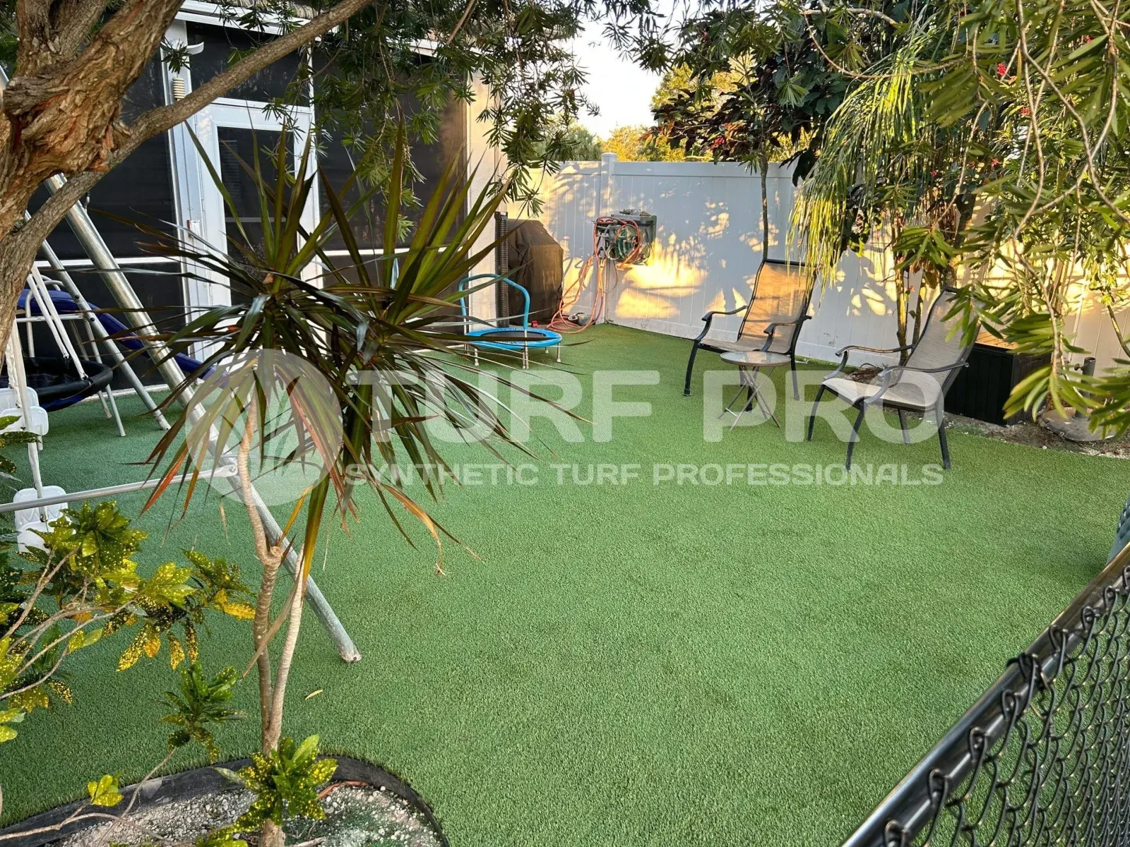 A small backyard with artificial turf and outdoor furniture under the trees.
