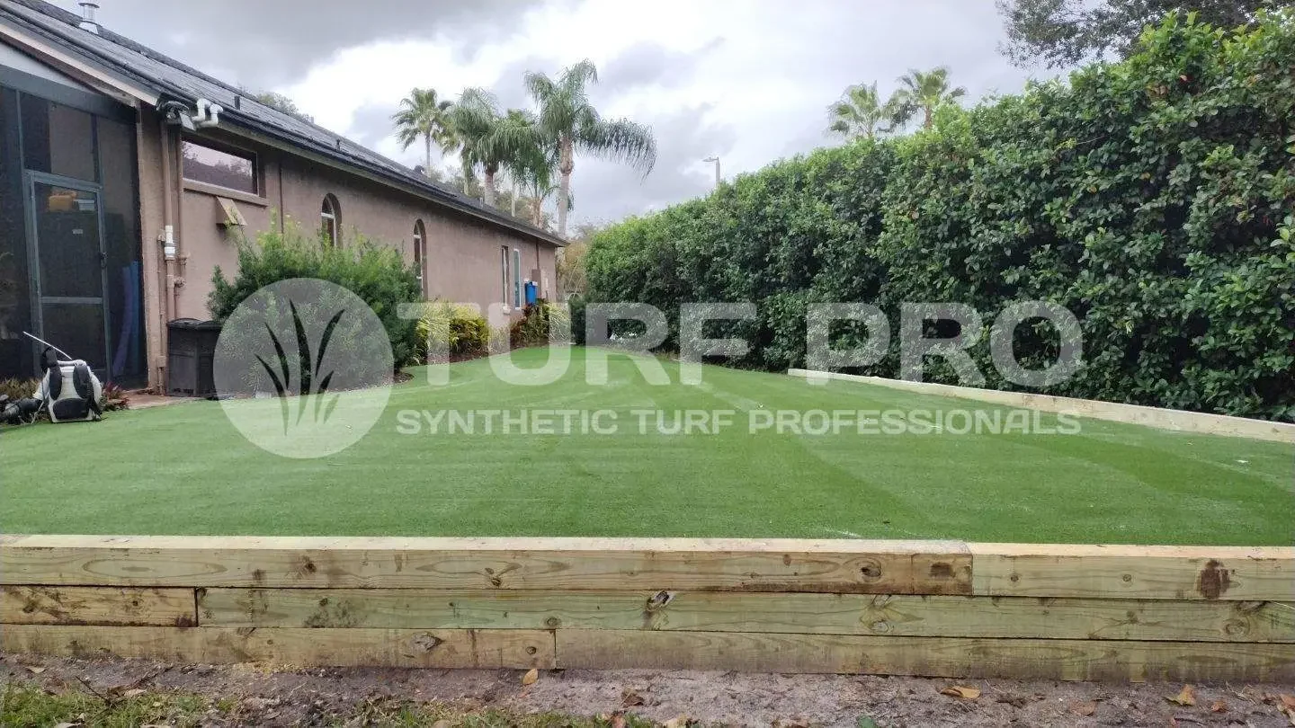 Freshly installed synthetic turf in a backyard with wooden edging.