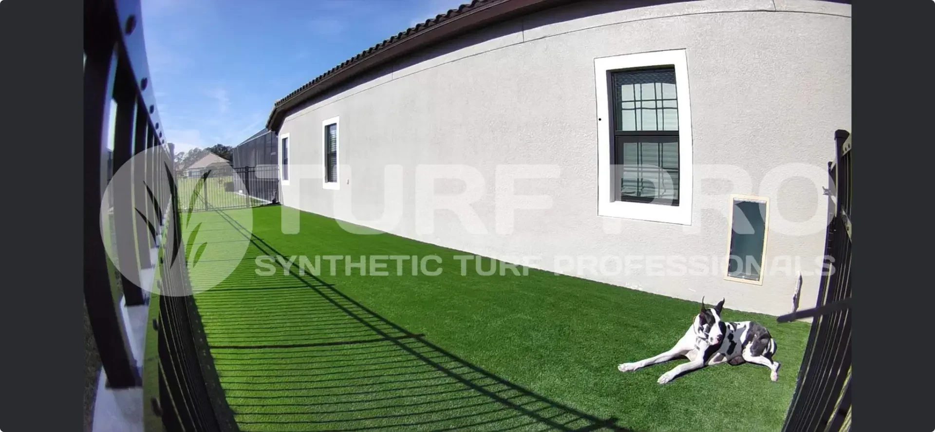Synthetic turf in a backyard next to a white house with a window.