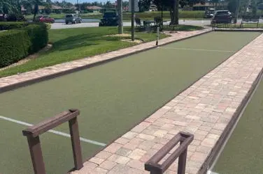 Outdoor bocce ball court with green playing surface and stone border.